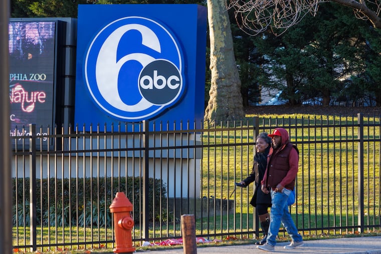 Two people walk by a 6abc sign outside their building at City Avenue and Monument in Philadelphia.
